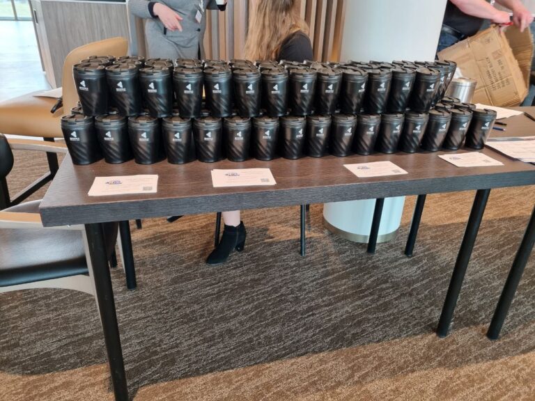 Photo of 100 brickfield branded travel coffee mugs neatly lined on a table in a conference room
