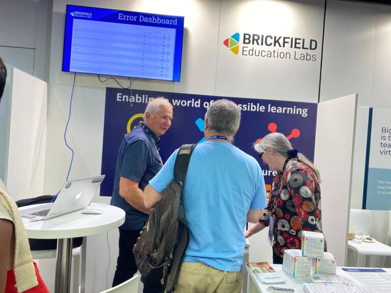 The Brickfield Education Labs Stand, with Karen and Mike Churchward talking to an interested potential customer. The stand banner reads Enabling a world of accessible learning. The monitor shows a screenshots of the Accessibility Toolkit displaying the Error Dashboard.